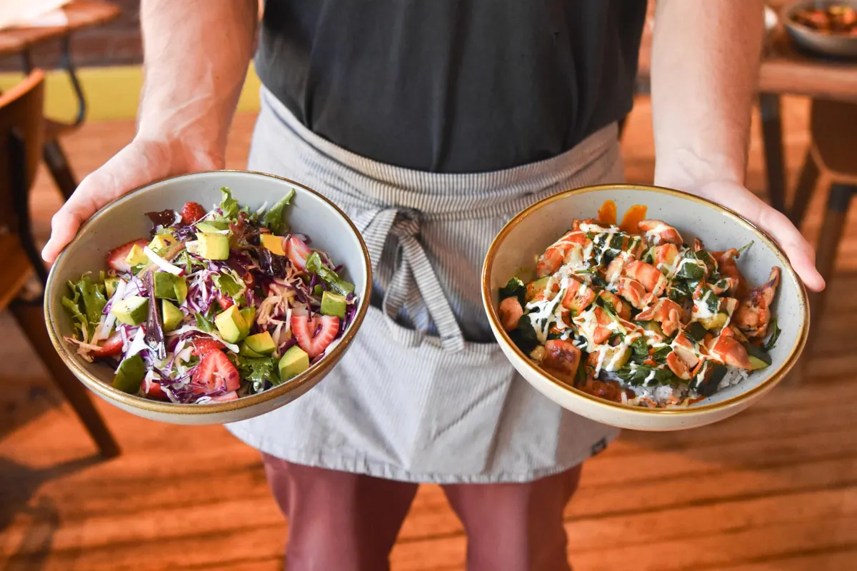 Server in an apron holding out two salad bowls