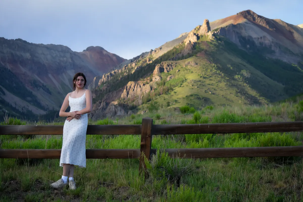 Young woman in a white dress by a wooden fence below red mountains